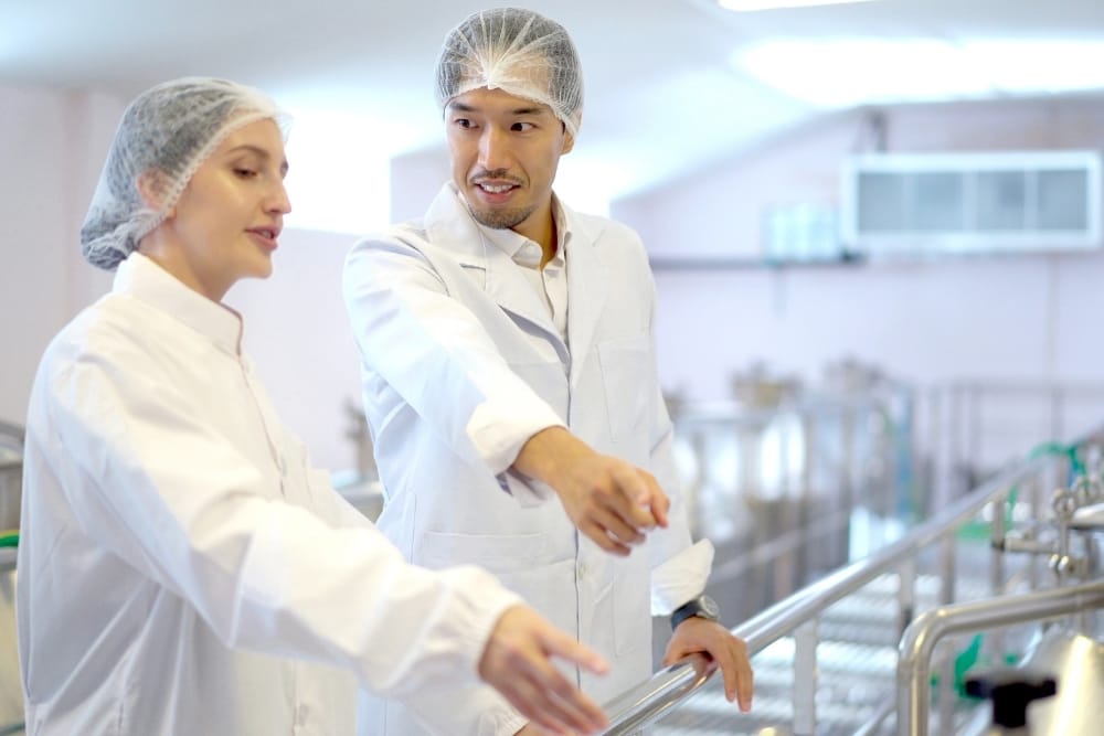Food and beverage market forecast UK: Food factory staff wearing protective clothing discussing production processes on a manufacturing line