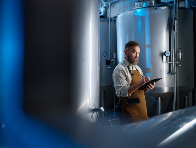UK food and beverage industry outlook 2026: Worker using a tablet to monitor equipment inside an industrial food processing facility