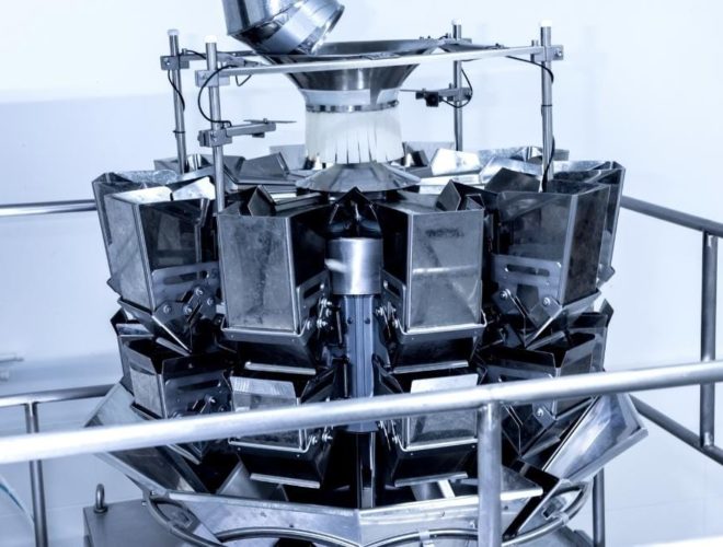 Bitesize learning in food production Close-up of a stainless steel multihead weigher machine used in food production, with multiple weighing buckets arranged in a circular formation.