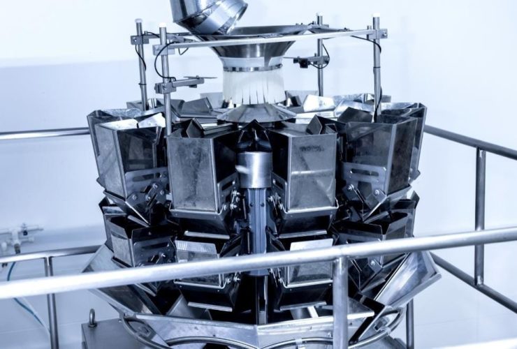 Bitesize learning in food production Close-up of a stainless steel multihead weigher machine used in food production, with multiple weighing buckets arranged in a circular formation.