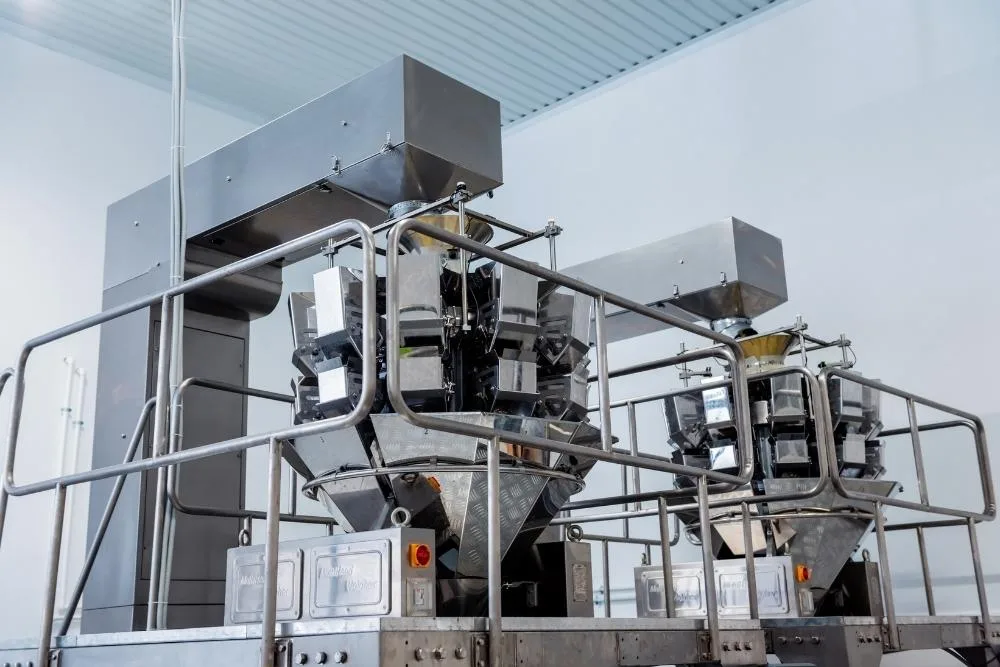 food production downtime: A large stainless steel multihead weigher machine in a clean, bright food production facility.