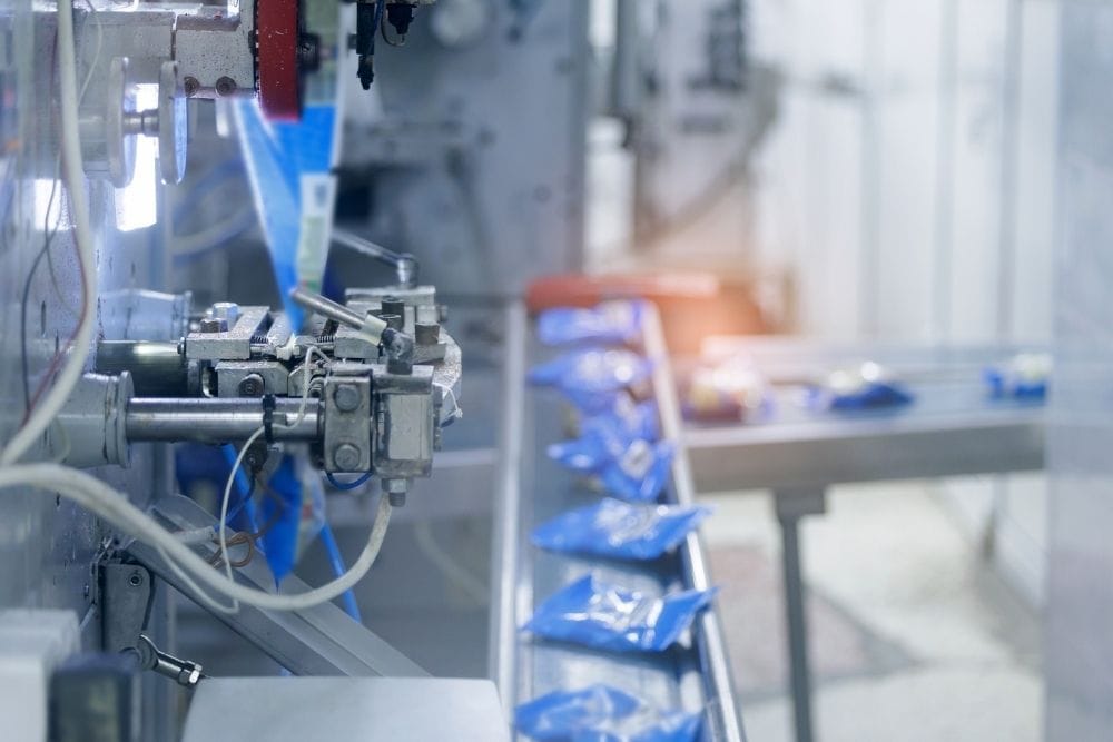 Food production line OEE: A close-up of automated packaging machinery on a food production line, with sealed blue packets moving along a conveyor belt.